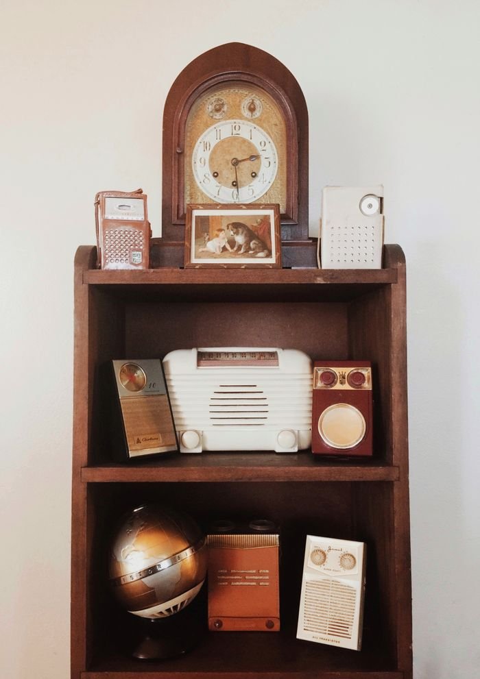 A collection of vintage radios and a globe on a wooden shelf with an antique clock.